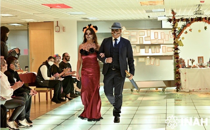Dos participantes con maquillaje de calavera y vestuario elegante en una pasarela del museo.
