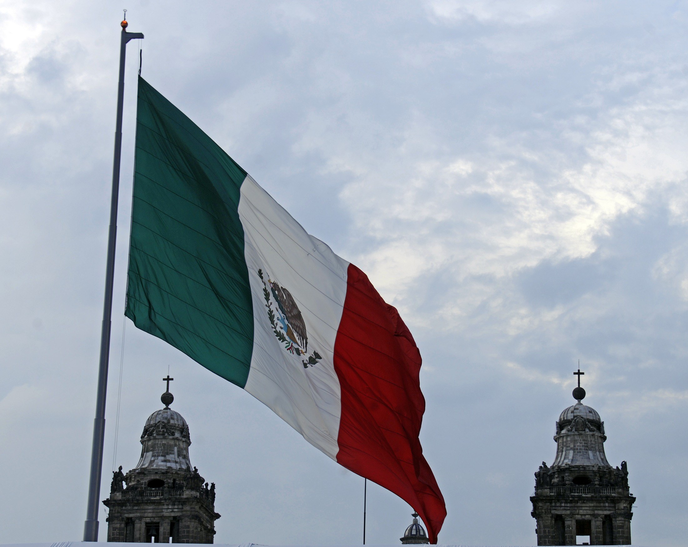 Bandera mexicana con el escudo, ondeando frente a las torres de la catedral.